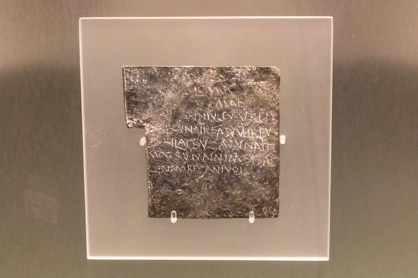 A small irregular sheet of grey lead covered in scratched Latin lettering.