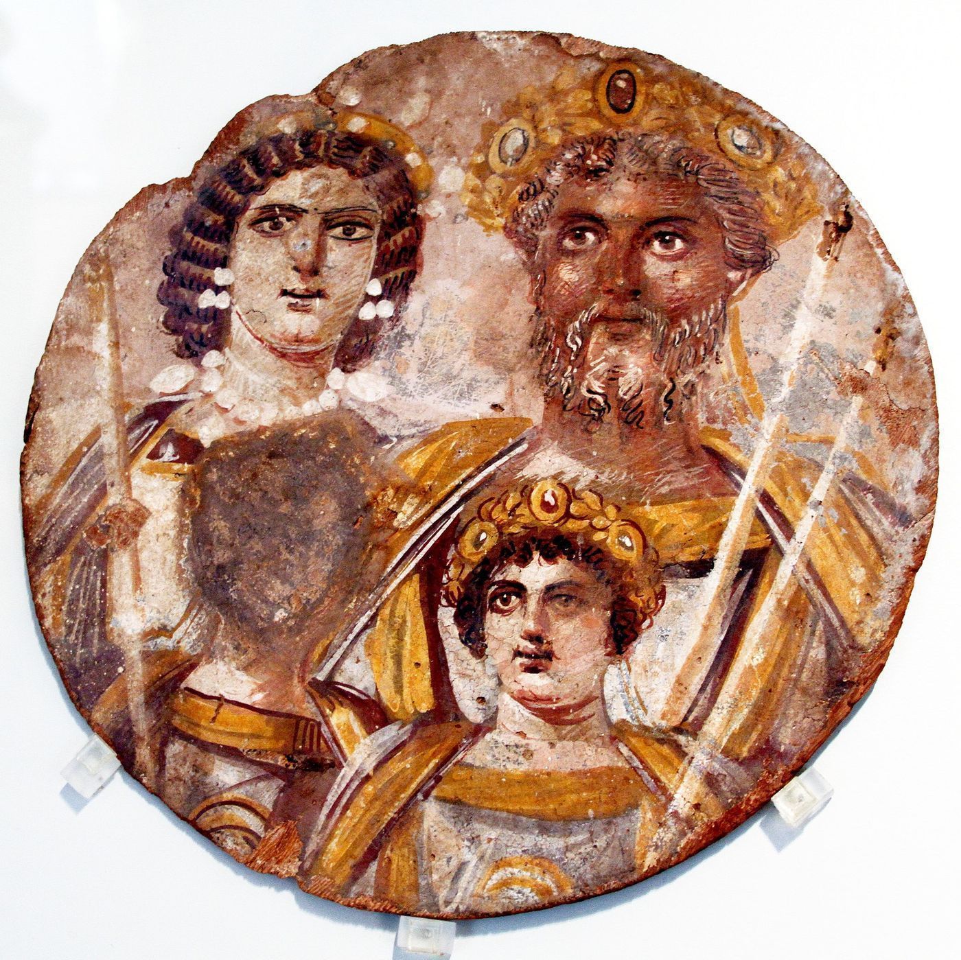 A circular painted panel showing the Roman imperial family, with the face of one of the two sons deliberately scraped away.