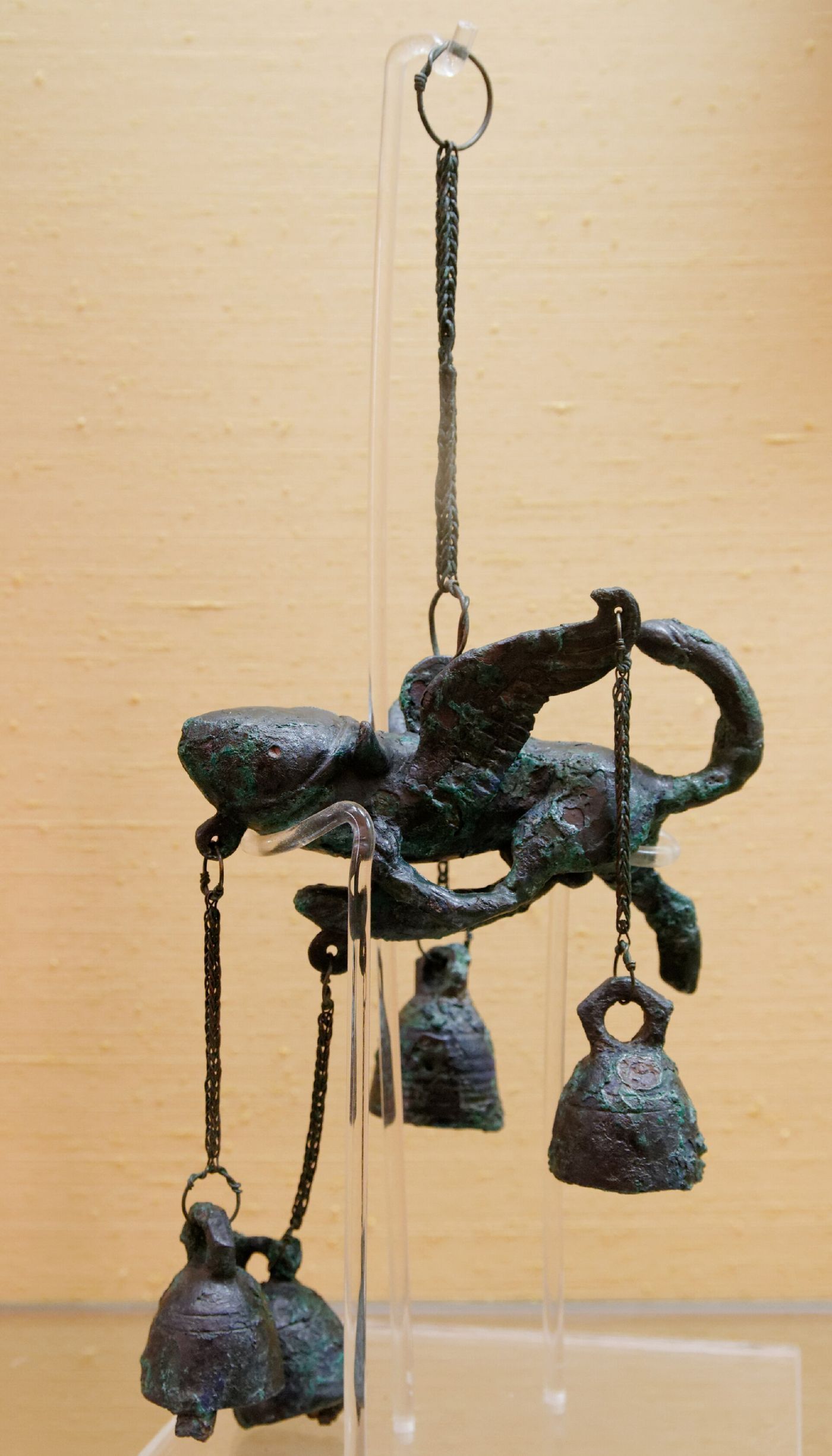 A bronze wind chime from Pompeii in the form of a winged phallus, with small bells suspended beneath it on chains.