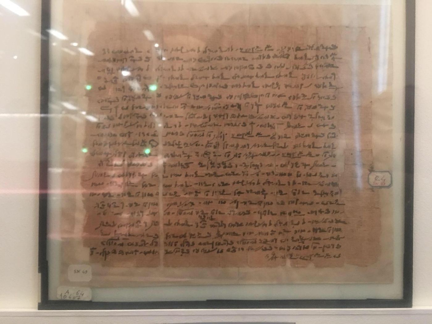A fragment of ancient papyrus densely written in Greek and Demotic script, with some lines picked out in red ink.