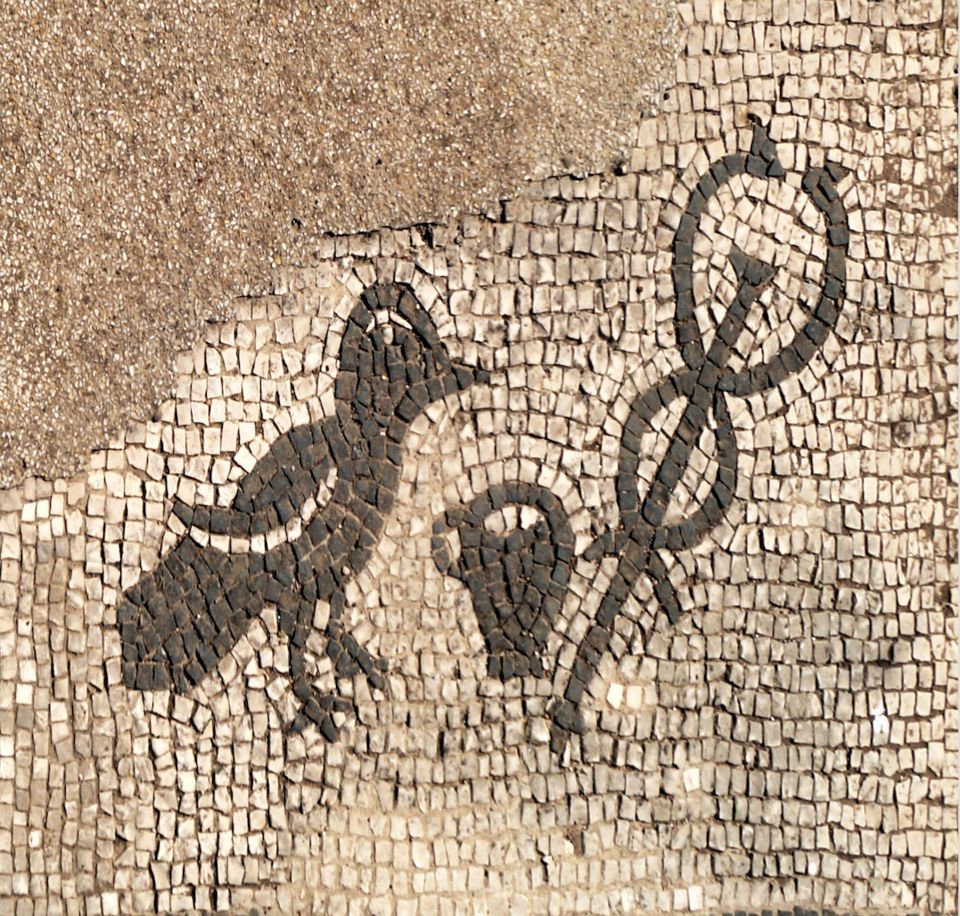 A black-and-white Roman mosaic panel showing a raven, a small drinking cup and a herald's staff, set in a plain border.