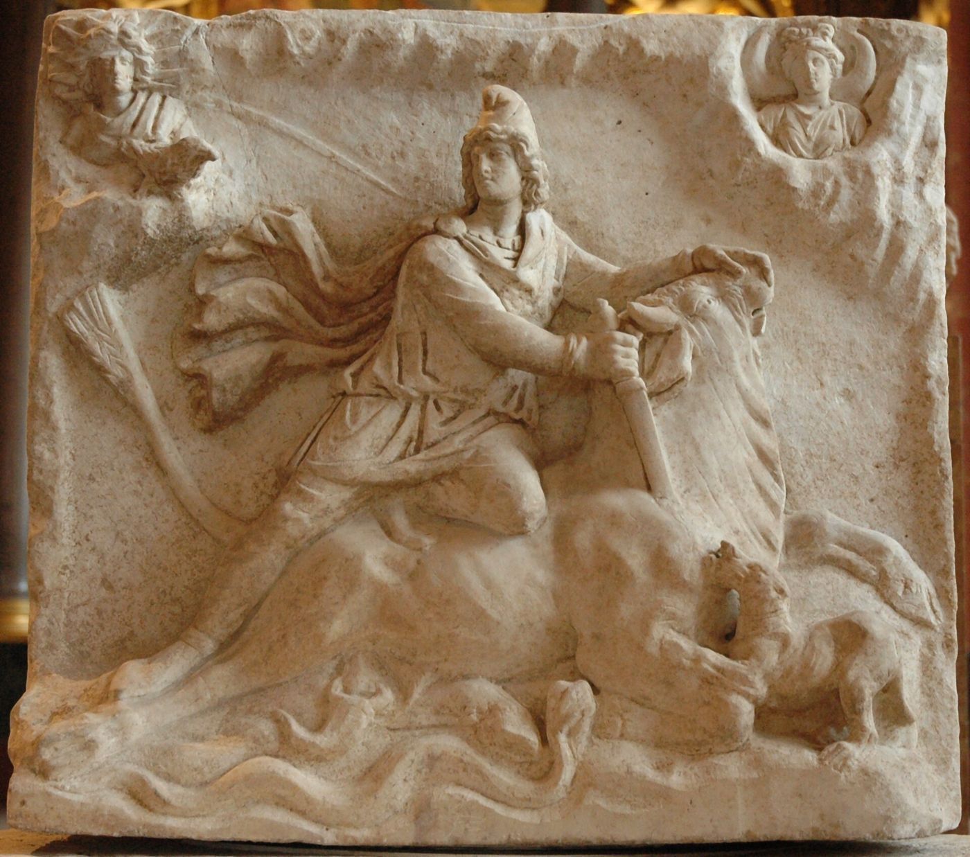 A carved marble relief of Mithras in a Phrygian cap kneeling on a bull and stabbing its neck, with a dog, snake and scorpion.